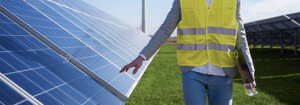 Trabajador con un peto amarillo fosforito, viendo las placas solares, impulsando la revolución verde y la reducción de emisiones en España.