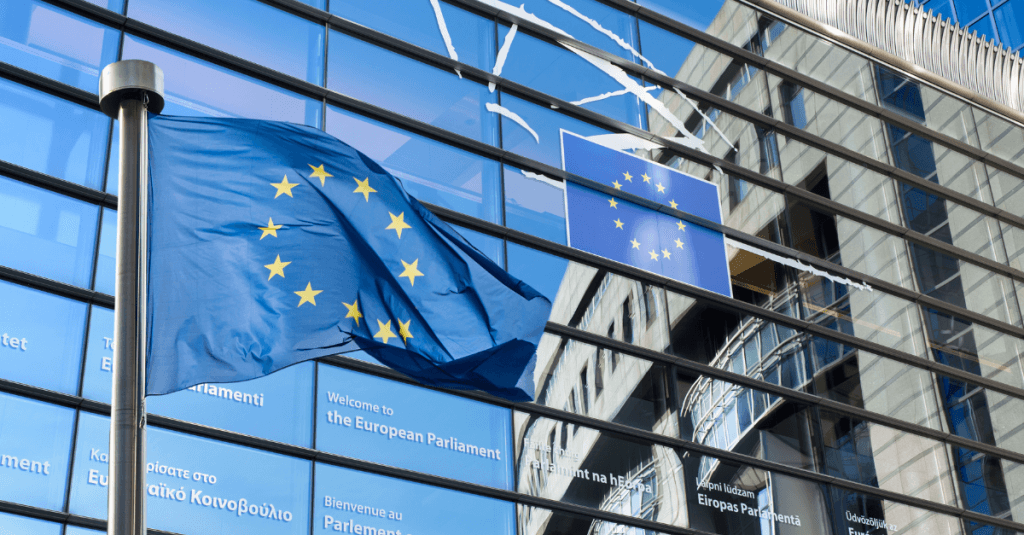 Bandera de la Unión Europea ondeando junto a un rascacielos corporativo, representando el Marco Financiero Plurianual 2028-2034.