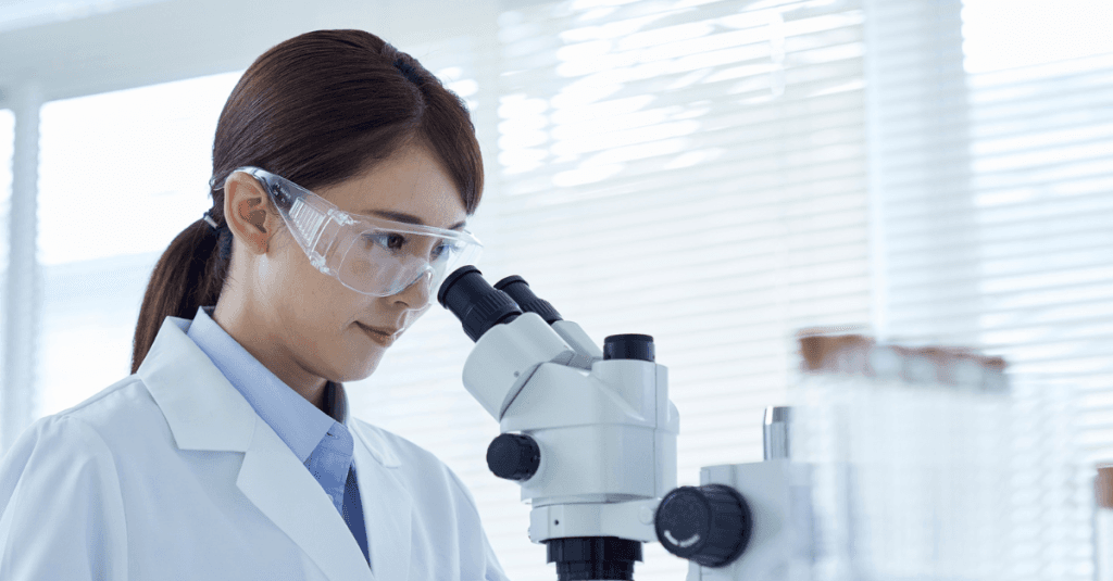 Mujer investigando en un laboratorio, observando muestras a través de un microscopio, en el contexto de fiscalidad en biotecnología.