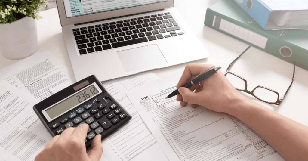 Persona trabajando en una mesa con ordenador y calculadora, analizando impuestos locales.
