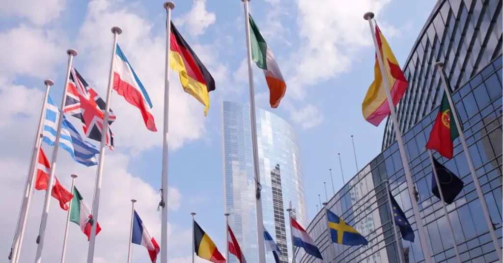 Banderas de países europeos frente a un edificio oficial de la UE, simbolizando los programas de financiación de la UE disponibles para proyectos empresariales y públicos.