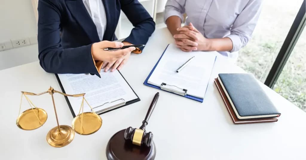 Reunión entre dos profesionales revisando documentación jurídica sobre la aplicación de un MASC, con una balanza y un mazo judicial sobre la mesa.